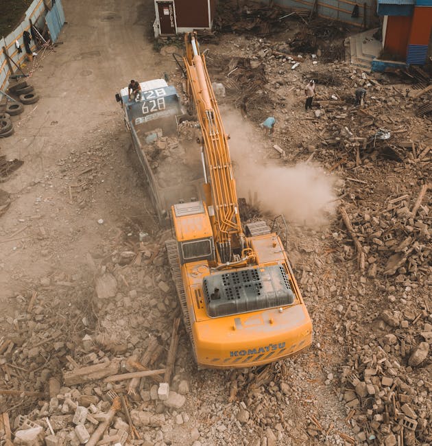 A scene of building debris and rubble outdoors at the base of a partially damaged multi-storey residential building. The foreground features broken bricks, concrete fragments, and scattered constructi